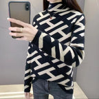 Femme portant un pull à col roulé noir et blanc à motifs géométriques, prenant un selfie avec un smartphone. Mode hiver, style moderne.