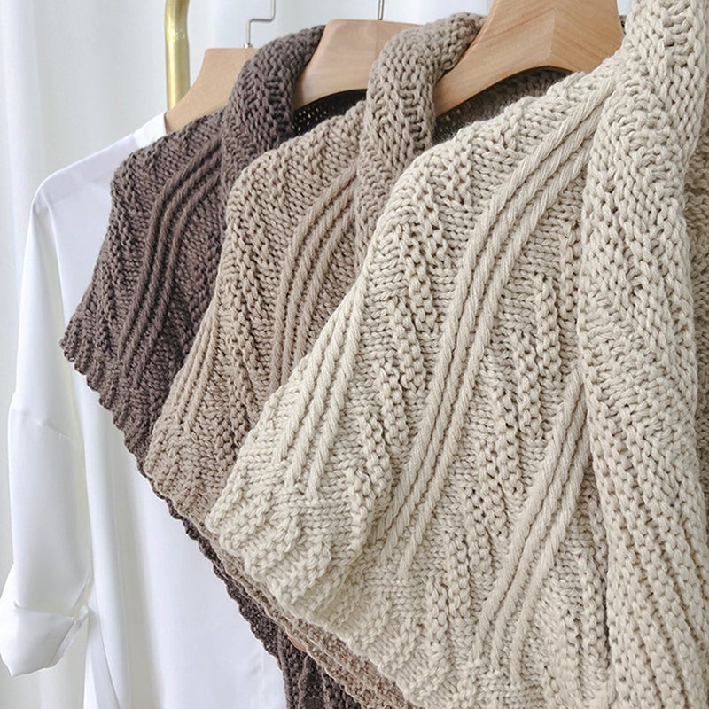 Trois pulls en tricot torsadé beige et marron suspendus sur des cintres en bois, exposés sur une chemise blanche. Mode hiver, vêtements chauds.