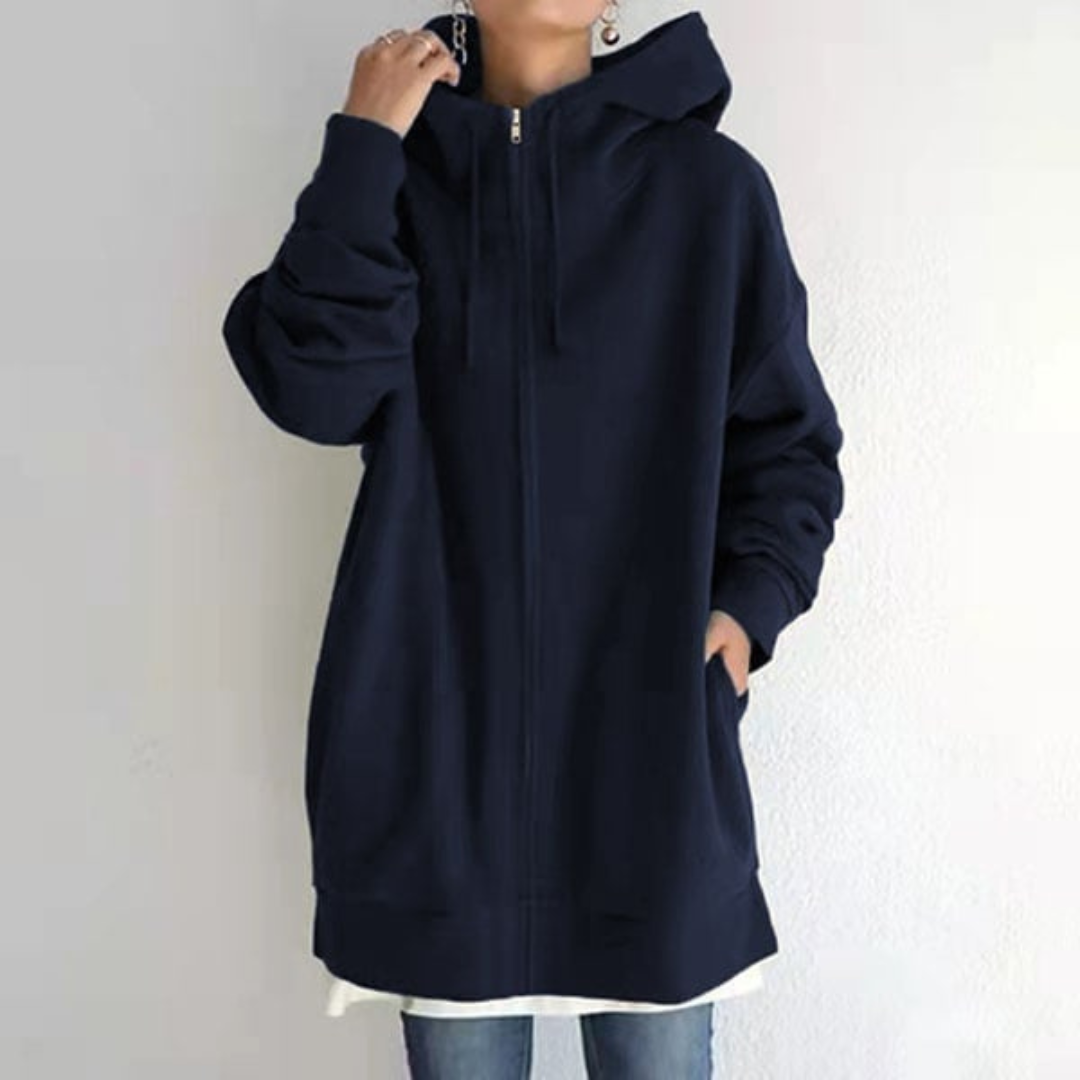 Veste à capuche zippée bleu marine, manches longues, portée par une personne debout, style décontracté, mode automne-hiver, tendance urbaine.