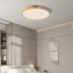 Plafonnier LED moderne rond en bois et rose, éclairant une chambre minimaliste avec lit blanc et décorations murales géométriques.