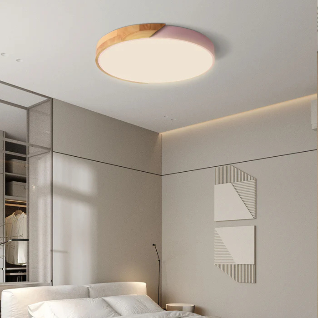 Plafonnier LED moderne rond en bois et rose, éclairant une chambre minimaliste avec lit blanc et décorations murales géométriques.