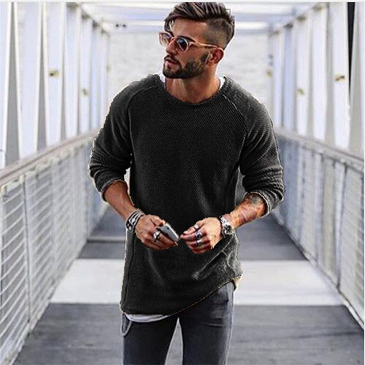 Homme moderne avec lunettes de soleil, pull noir, jeans, posant sur un pont urbain. Mode masculine, style décontracté, accessoires tendance.
