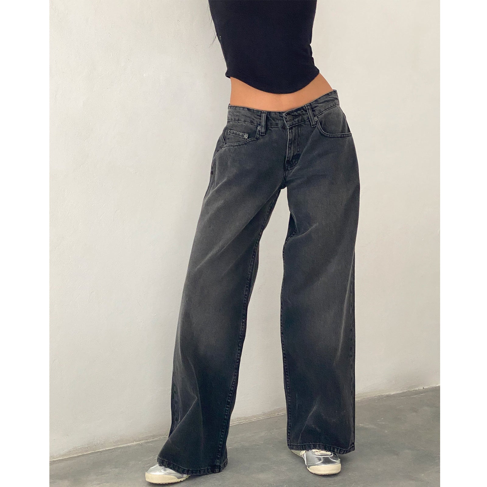 Jeans larges noirs taille haute, portés par une femme en haut noir, posant contre un mur blanc. Mode décontractée, tendance streetwear.