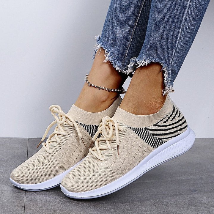 Baskets beiges en maille respirante avec lacets, portées avec un jean déchiré. Chaussures de sport tendance pour femme, confort et style.