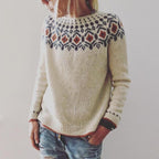 Femme portant un pull en laine beige avec motif nordique coloré, manches longues, col rond, associé à un jean décontracté. Mode hiver tendance.