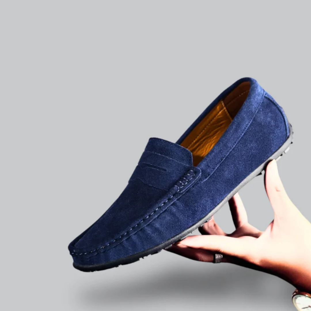 Mocassin bleu en daim pour homme, élégant et confortable, tenu par une main. Chaussure mode, semelle antidérapante, idéale pour un look décontracté.