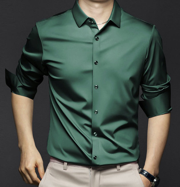 Homme portant une chemise en satin vert foncé, manches retroussées, sur fond noir. Mode masculine élégante, tenue chic et moderne.