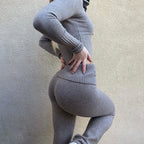 Femme en tenue moulante grise, pose de profil contre un mur beige, mettant en valeur la mode athlétique et le style décontracté.