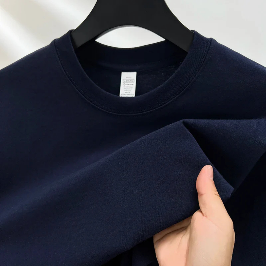 Sweat-shirt bleu marine en coton, suspendu sur un cintre noir, avec une main tenant le tissu. Mode décontractée, vêtement basique, style minimaliste.