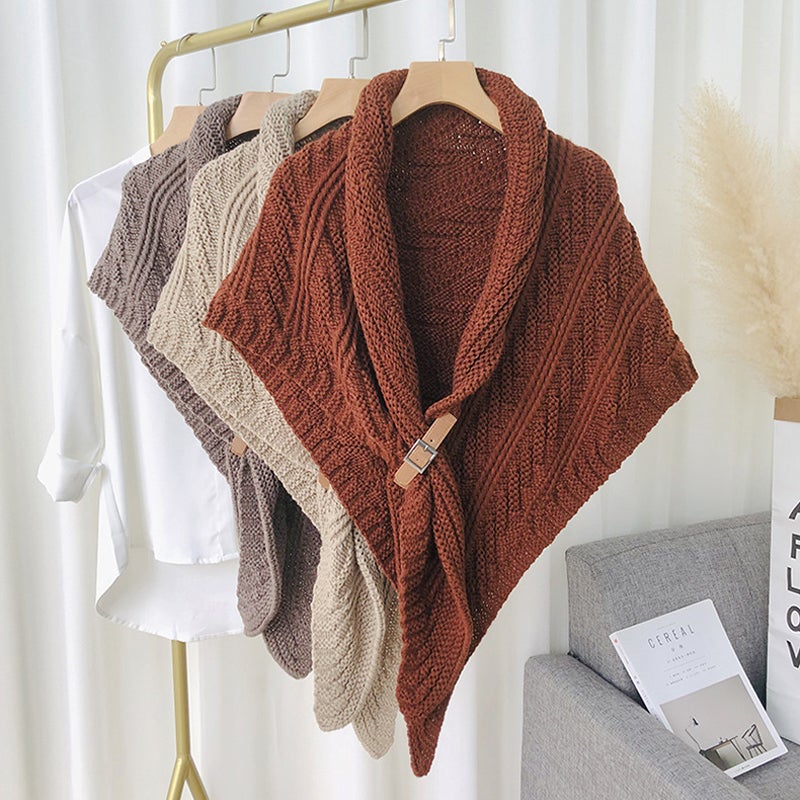 Ponchos en tricot torsadé suspendus sur cintres, couleurs marron, beige et taupe, sur fond de rideau blanc. Mode automne-hiver, vêtements chauds.