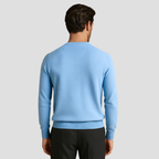 Homme portant un pull bleu clair en laine mérinos, vu de dos, sur fond gris. Mode masculine élégante, tenue automne-hiver, style décontracté.