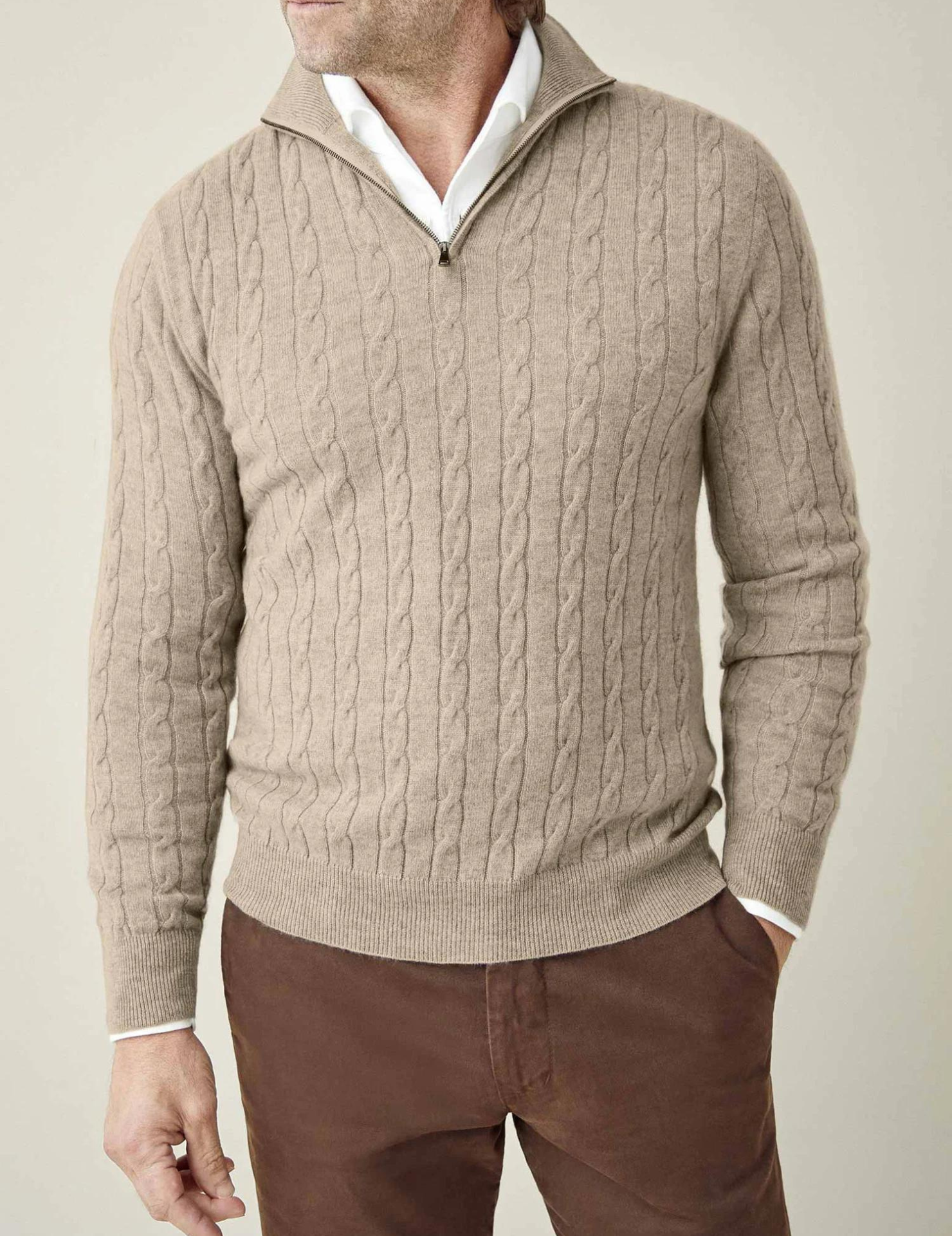 Homme portant un pull torsadé beige avec col zippé, chemise blanche en dessous, pantalon marron. Mode masculine élégante et décontractée.