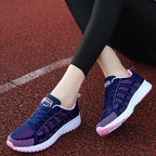 Baskets de course bleues et roses pour femme sur piste rouge, design moderne, semelle blanche, confortables et légères, idéales pour le sport.