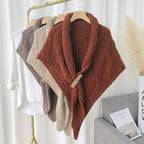 Châles en tricot épais suspendus sur cintres, couleurs marron, beige et taupe, sur fond de rideau blanc. Accessoires mode automne-hiver.