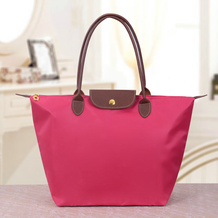Sac à main rose vif avec poignées marron, posé sur une table. Design élégant, idéal pour la mode féminine. Accessoire tendance et pratique.