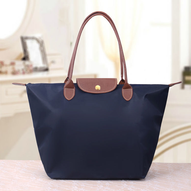 Sac à main bleu marine avec poignées marron, posé sur une table. Design élégant et pratique, idéal pour la mode féminine et le quotidien.
