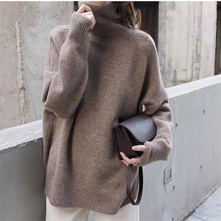 Femme portant un pull en laine marron avec un col roulé, tenant un sac à main en cuir marron foncé, style automne-hiver, mode urbaine élégante.