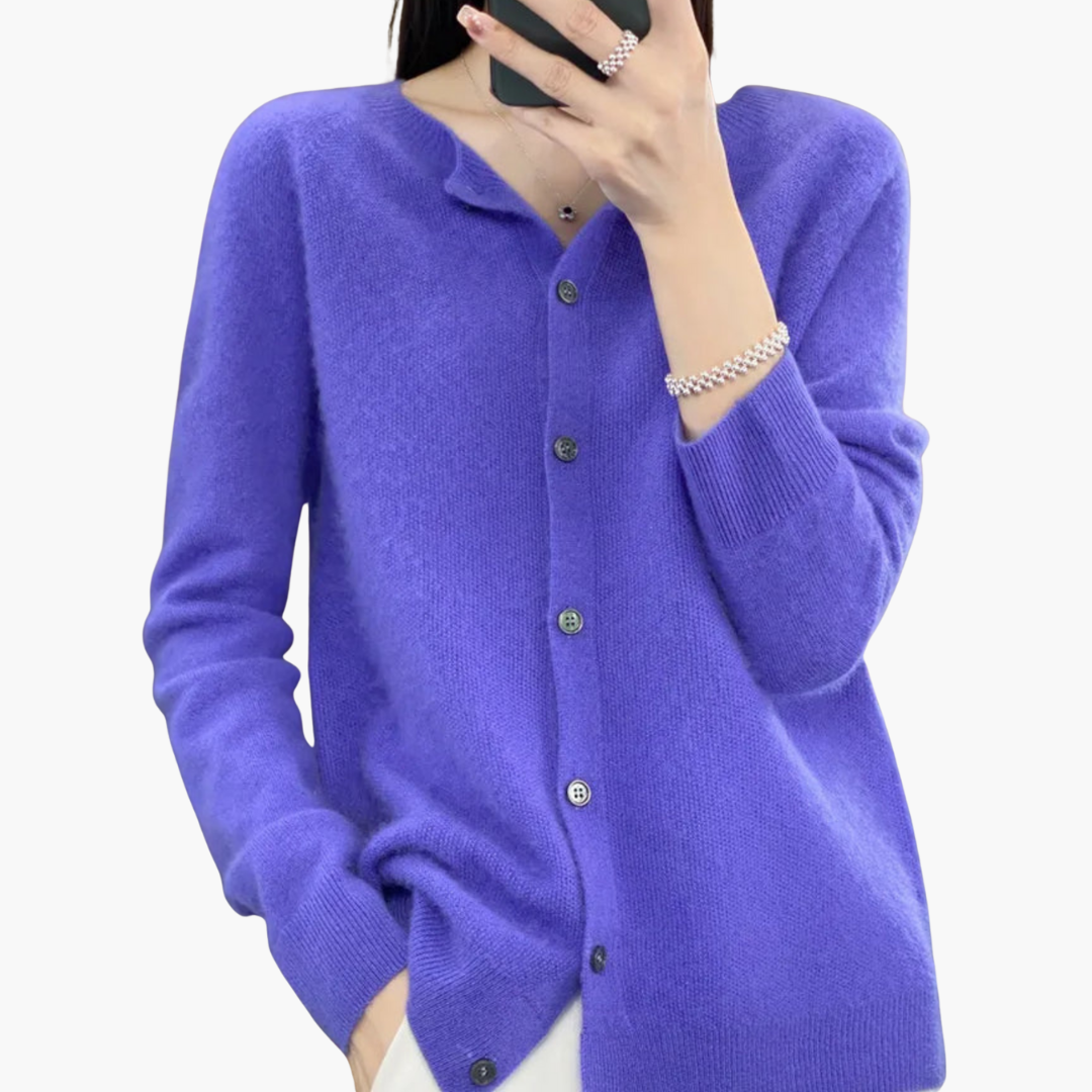 Femme portant un cardigan violet en cachemire avec boutons noirs, bracelet argenté, et bague, sur fond blanc. Mode élégante et confortable.
