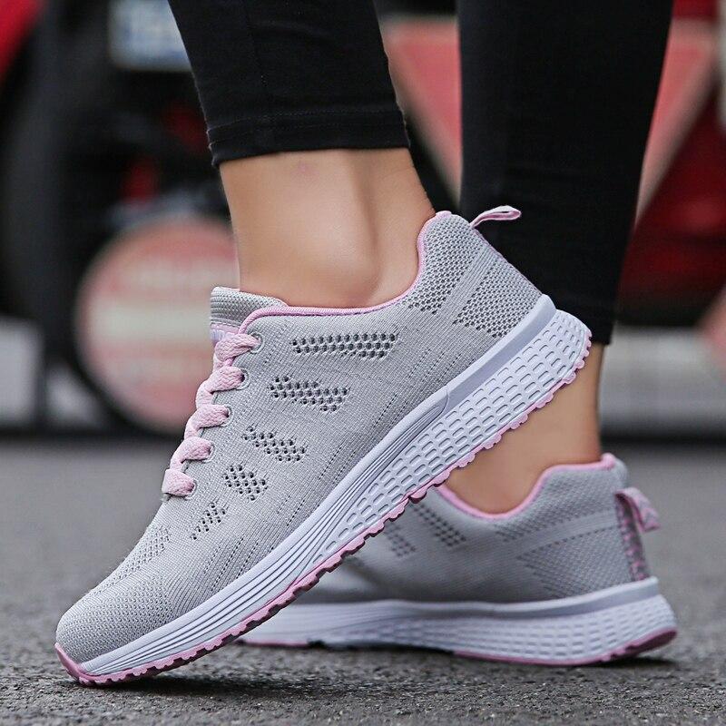 Chaussures de sport femme grises avec lacets roses, semelle blanche antidérapante, portées sur route. Idéales pour course à pied et fitness.