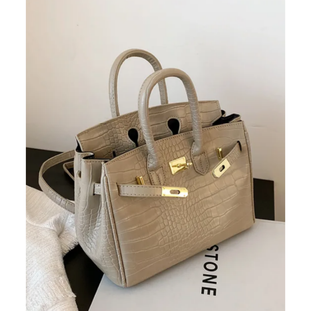Sac à main beige en cuir texturé crocodile, style Birkin, avec fermoir doré, posé sur une boîte blanche. Accessoire mode élégant et tendance.