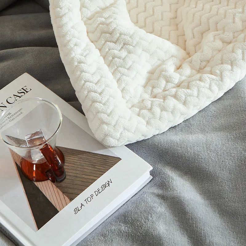 Couverture en laine blanche texturée sur un livre de design moderne avec une tasse en verre, posée sur un drap gris. Décoration intérieure élégante.