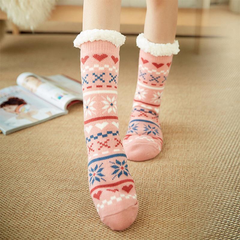 Chaussettes roses en laine avec motifs nordiques, cœurs et flocons de neige, portées sur un tapis beige. Accessoire hiver confortable et tendance.