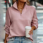 Femme portant un pull rose côtelé avec fermeture éclair, tenant un gobelet de café à emporter, style décontracté, mode automne-hiver tendance.