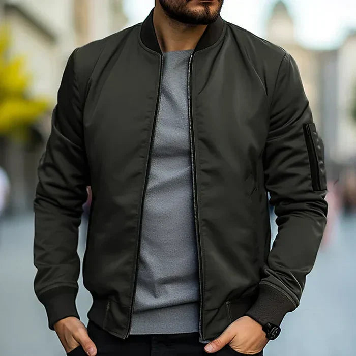 Homme portant un blouson bomber noir, t-shirt gris, dans une rue urbaine floue. Mode masculine, style décontracté, tendance automne.