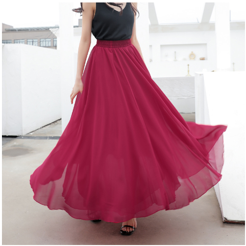 Femme en jupe longue rouge fluide, top noir, posant sur une terrasse moderne. Mode féminine élégante, style urbain chic, vêtements tendance.