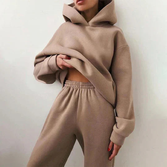 Femme portant un ensemble de survêtement beige, composé d'un sweat à capuche ample et d'un pantalon de jogging, style décontracté et tendance.