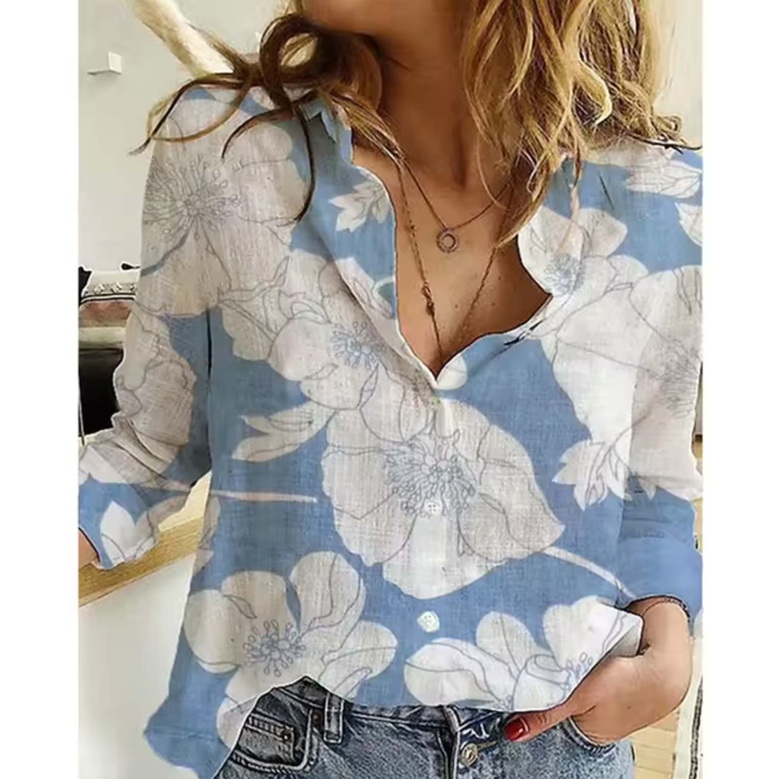 Chemisier femme à fleurs blanches sur fond bleu, manches longues, col en V, porté avec un jean. Mode féminine, style décontracté, tendance printemps.