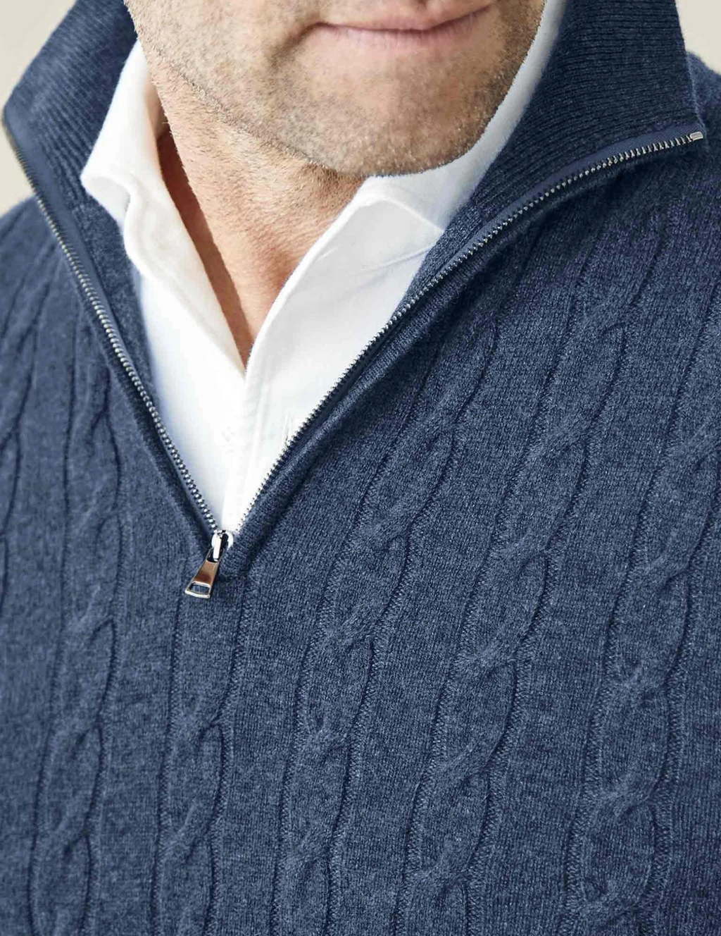 Homme portant un pull bleu à col zippé en maille torsadée sur une chemise blanche. Mode masculine élégante, tenue automne-hiver.