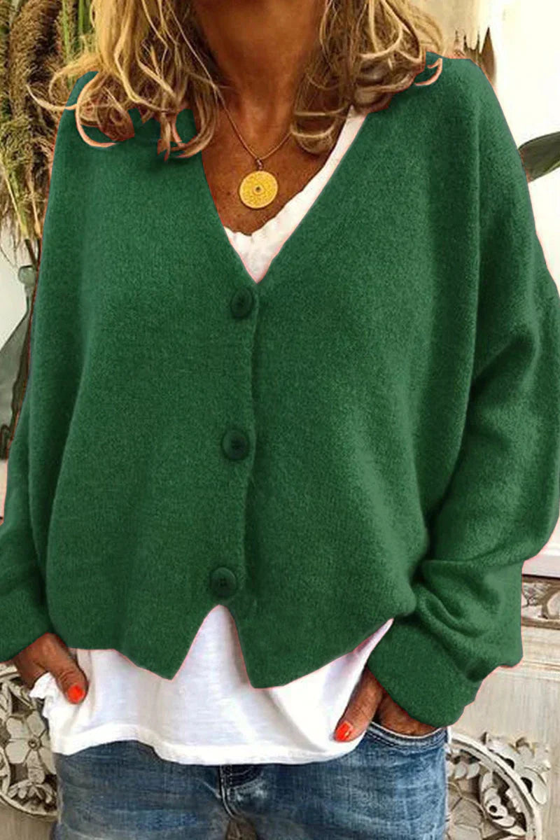 Femme portant un cardigan vert en laine avec boutons, sur un t-shirt blanc, et un collier doré. Mode automne, style décontracté, tendance féminine.