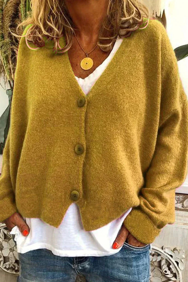 Femme portant un cardigan en laine jaune moutarde avec boutons, sur un t-shirt blanc, et un collier doré, style décontracté automne-hiver.