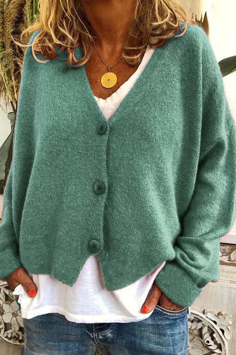 Femme portant un cardigan vert en laine avec boutons, sur un t-shirt blanc, et un collier doré. Mode décontractée, style automne-hiver.