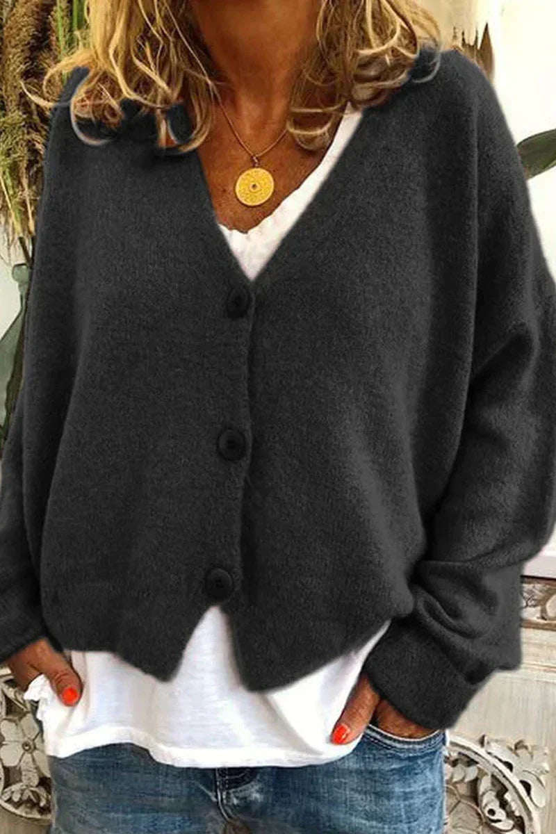 Femme portant un cardigan en laine gris foncé avec boutons, sur un t-shirt blanc, et un collier doré. Mode automne, style décontracté.