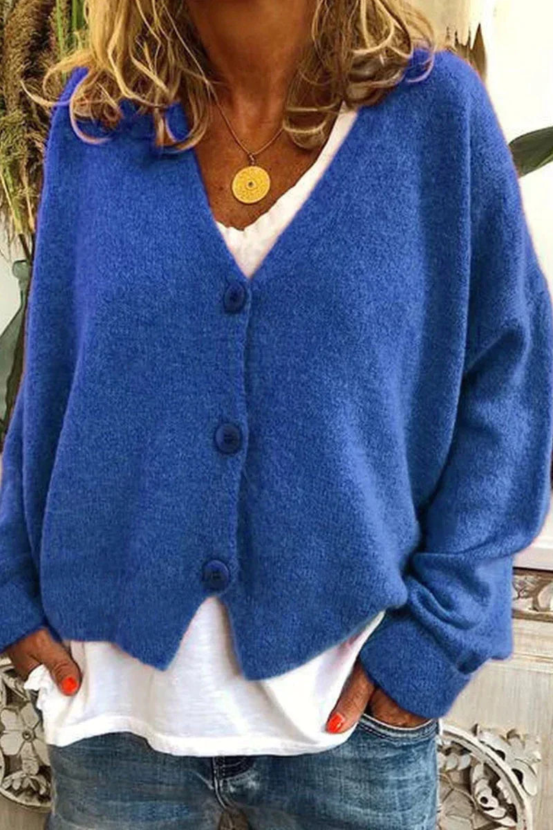 Femme portant un cardigan bleu en laine avec boutons, sur un t-shirt blanc, et un collier doré. Mode automne, style décontracté, tendance féminine.