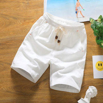 Short en lin blanc pour homme sur une table en bois, avec cordon de serrage et poches. Style décontracté estival, idéal pour la plage ou les loisirs.