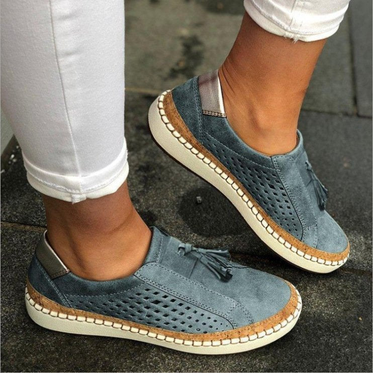 Chaussures en daim bleu avec semelle blanche et détails tressés, portées avec un pantalon blanc. Style décontracté et moderne pour femme.