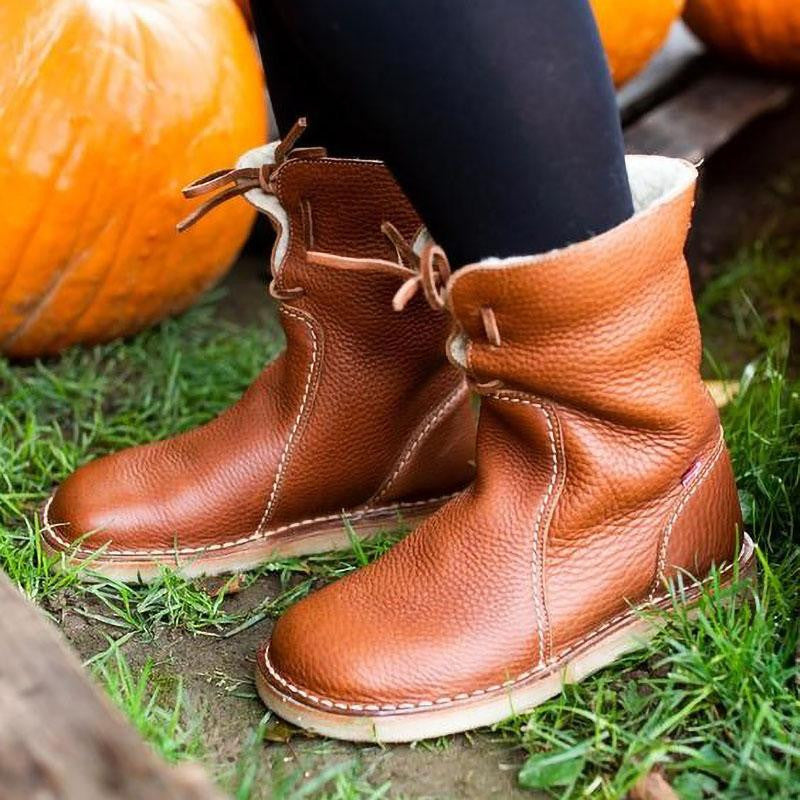 Bottes en cuir marron pour femme sur herbe verte, avec citrouilles en arrière-plan. Chaussures automne confortables, style décontracté.