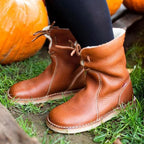 Bottes en cuir marron pour femme sur herbe verte, avec citrouilles en arrière-plan. Chaussures automne confortables, style décontracté.
