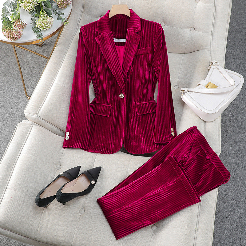 Costume en velours rouge pour femme, posé sur un canapé beige, accompagné de chaussures noires et d'un sac à main blanc. Mode élégante et tendance.