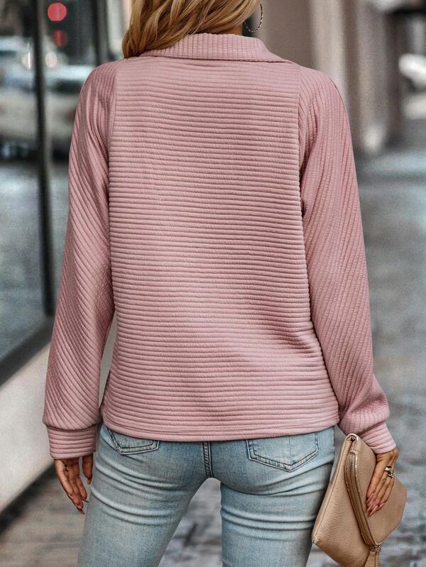 Femme portant un pull rose texturé et un jean bleu clair, tenant une pochette beige. Mode féminine, tenue décontractée, style urbain.