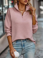 Femme portant un pull rose à col zippé et un jean bleu, tenant un gobelet de café. Mode décontractée, style urbain, tenue automne-hiver.
