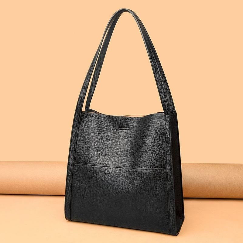 Sac à main en cuir noir élégant avec longues anses, design minimaliste, posé sur fond beige. Accessoire mode femme, tendance et chic.