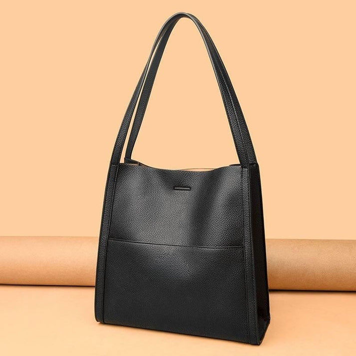 Sac à main en cuir noir élégant avec longues anses, design minimaliste, fond beige. Accessoire mode femme, tendance et chic.