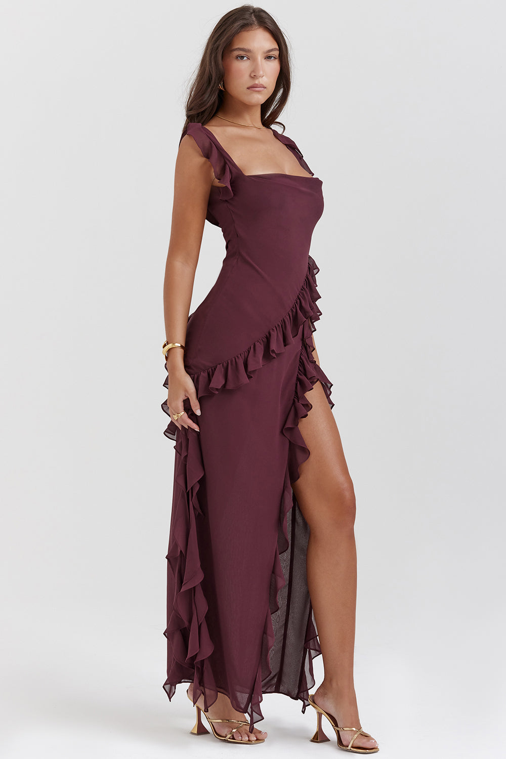 Robe longue bordeaux élégante avec volants, fente haute, portée par une femme. Mode féminine, tenue de soirée chic, style glamour.