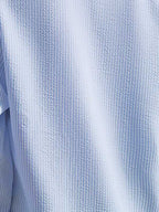 Chemise en seersucker bleu clair, texture gaufrée, tissu léger et respirant, idéal pour l'été, mode homme élégante et décontractée.