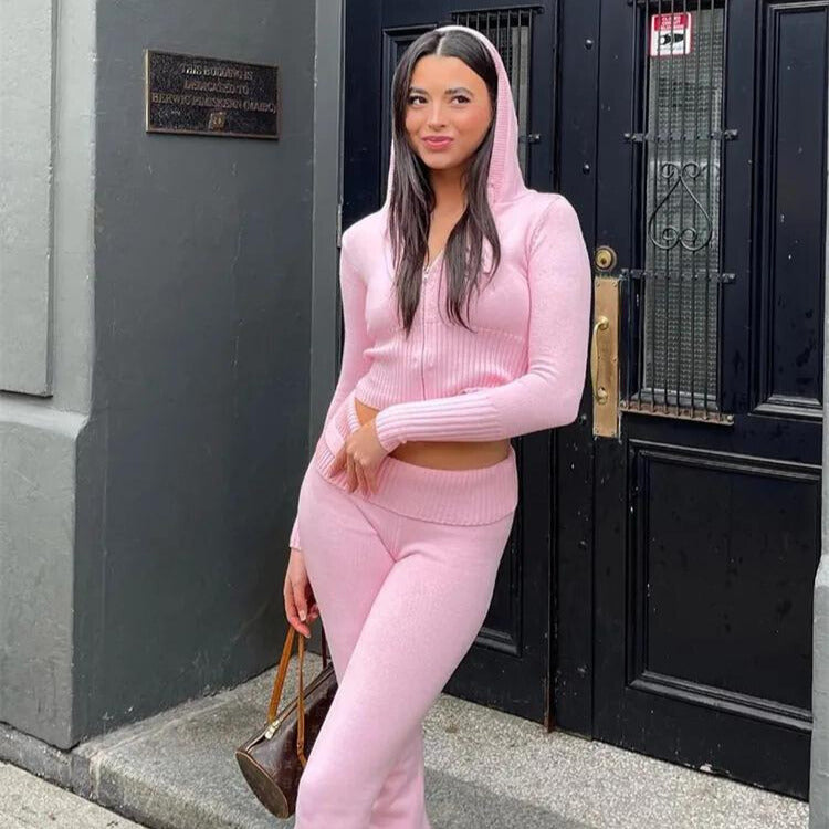 Jeune femme en ensemble rose, pose devant une porte noire, tenant un sac à main marron. Mode féminine, tenue décontractée, style urbain.
