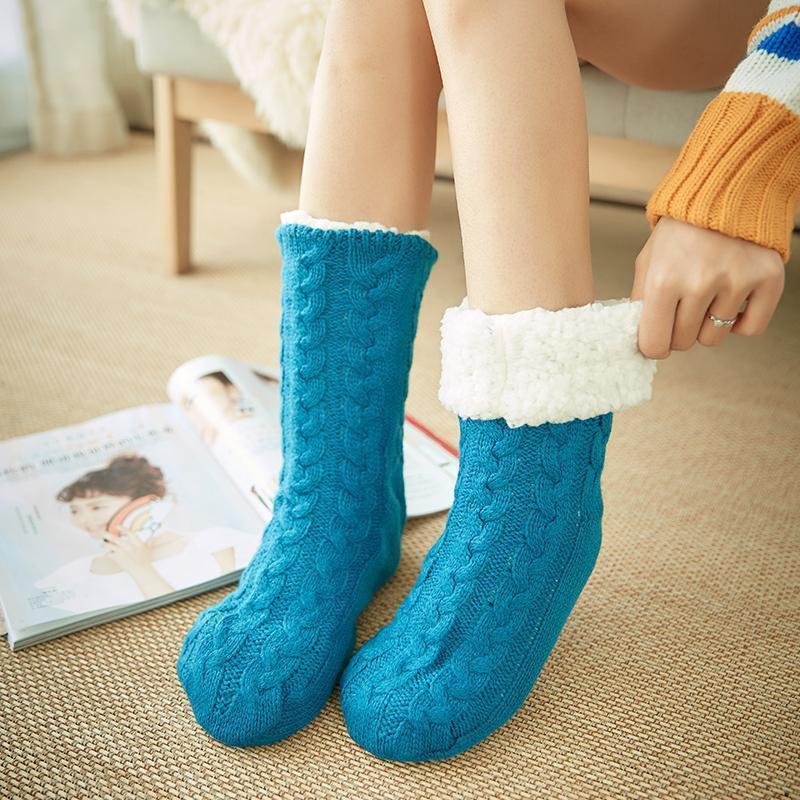 Chaussettes en laine bleue avec doublure en fourrure blanche, portées par une personne assise sur un canapé, magazine ouvert en arrière-plan.